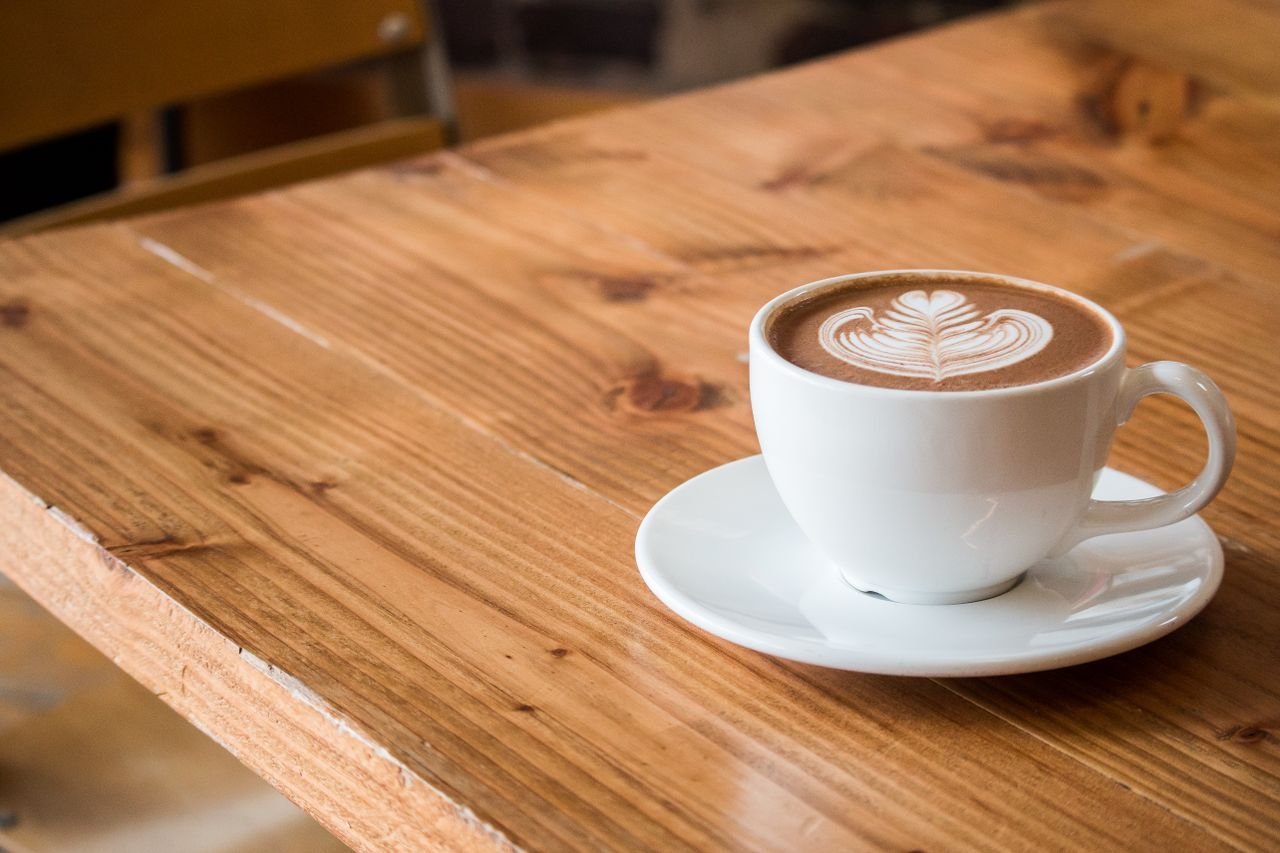 Home Close-up of a white cup of latte with artistic foam on a rustic wooden table.